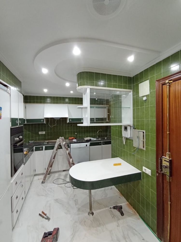 Cocina en plena reforma, con azulejos verdes y falso techo con focos